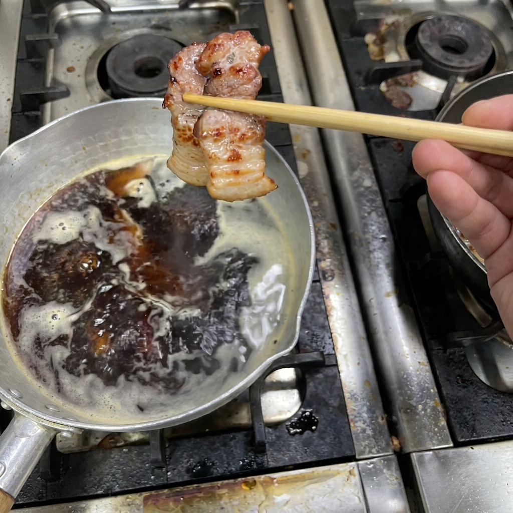 A piece of browned, cooked pork belly held by chopsticks over a simmering pot of dark sauce.