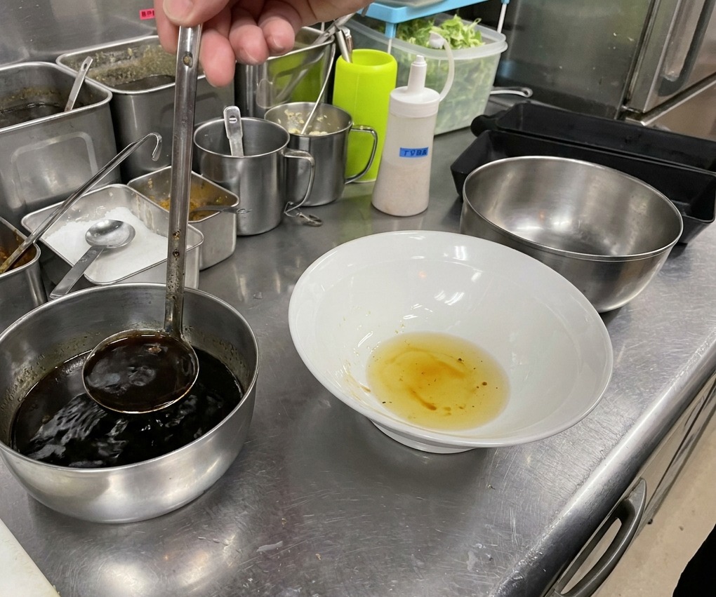 Dark soy sauce being ladled into a white bowl that already contains a layer of golden oil.