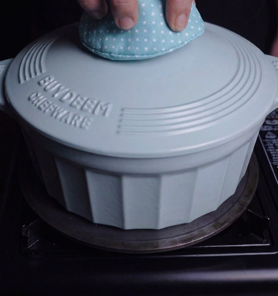 A person using a polka-dot oven mitt to place a light blue lid onto a matching enamel pot on a stovetop.