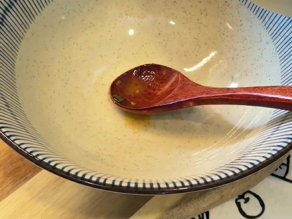 Creamy orange-tinted broth being poured from a small bowl into a large ceramic serving bowl with blue and white stripes.