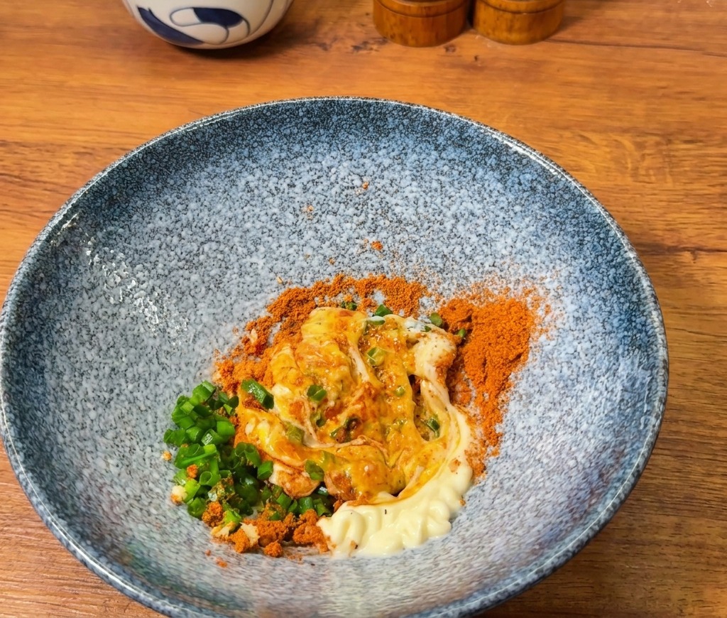 A blue bowl containing an orange seasoning mixture being combined with a thick white dollop of mayonnaise.