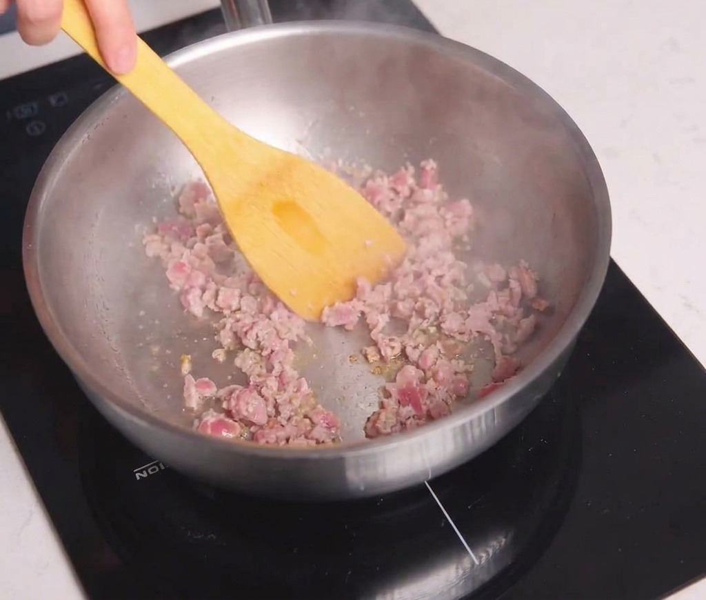 Ground meat being broken up and stir-fried in a pan with a yellow spatula until it reaches a browned consistency.
