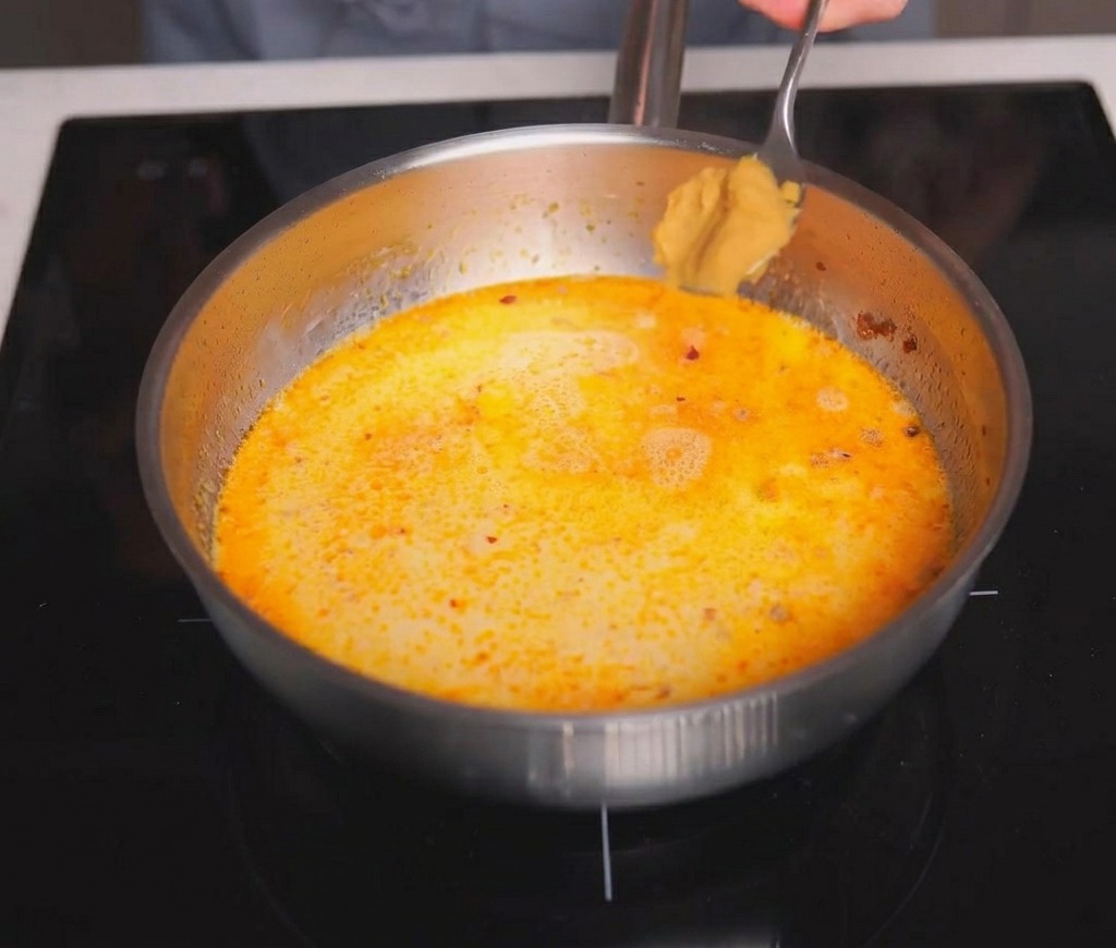 A spoonful of light brown miso paste being added to a pan of simmering creamy soup broth.