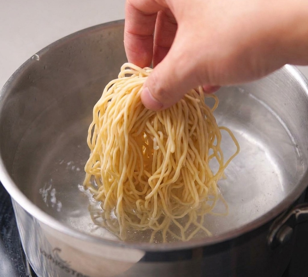 A stainless steel pot filled with water on a stovetop with small bubbles forming at the base of the pot.