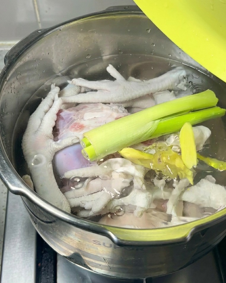 Fresh green scallions and ginger slices resting on top of the raw meat and water inside a cooking pot.