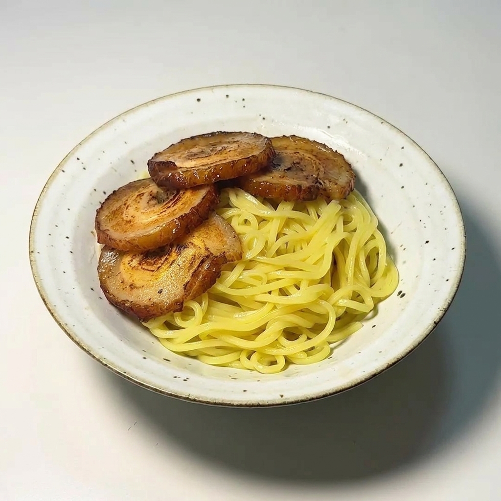 Four slices of browned, seared chashu pork arranged neatly over a bed of yellow ramen noodles in a white bowl.
