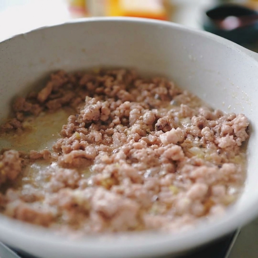 Minced pork and shredded white onions being stir-fried together in a light-colored pan.