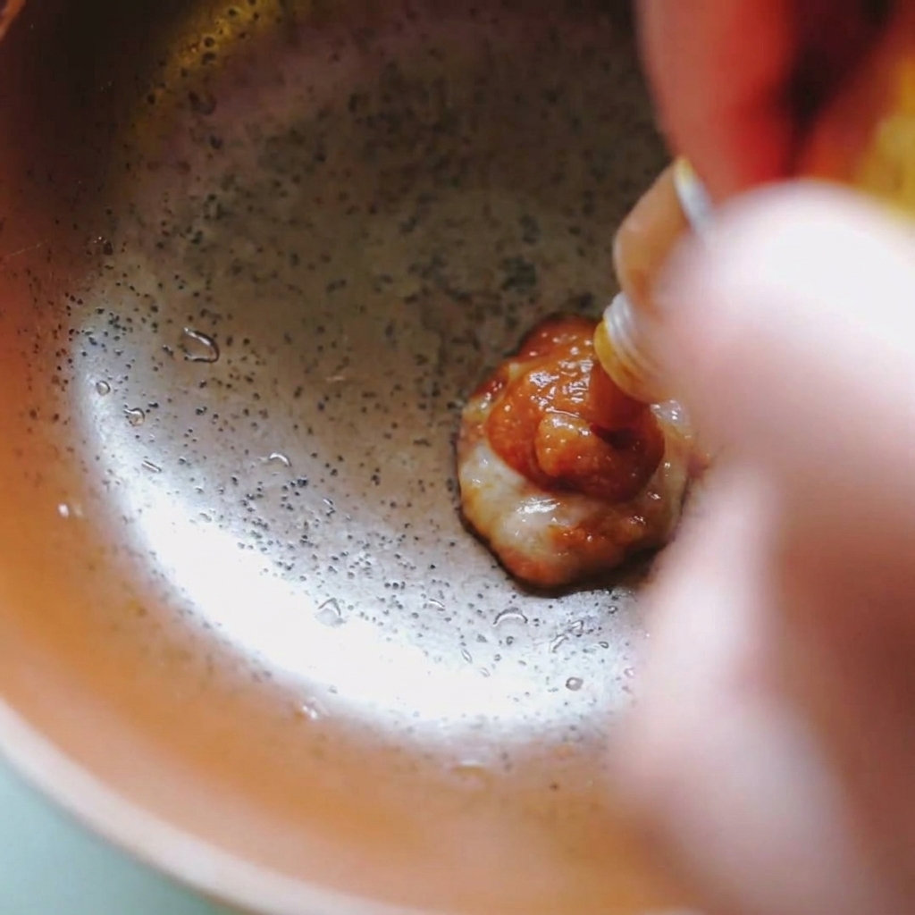 Thick brown miso paste being squeezed from a small white and yellow packet into a brown ceramic bowl.