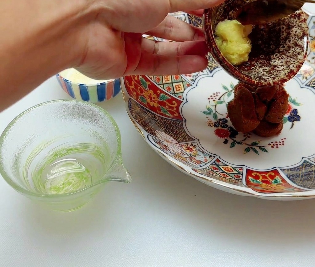 A small portion of yellow minced ginger paste being added to a mound of brown miso in a ceramic bowl.