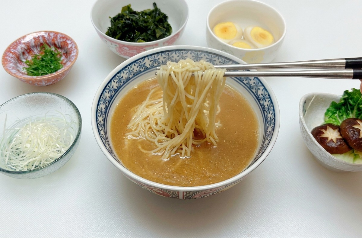 A pair of silver chopsticks lifting and centering cooked ramen noodles within a bowl of brown miso broth.
