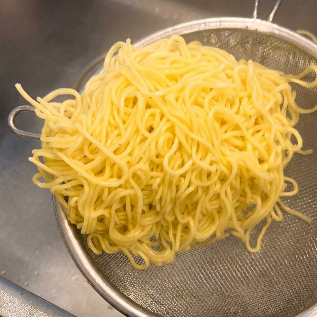 Cooked yellow ramen noodles sitting in a metal mesh strainer being shaken to remove excess water.