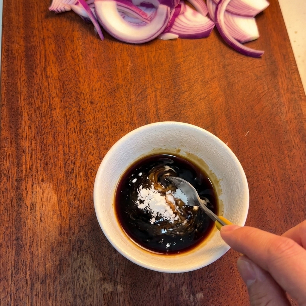 A spoon stirring a dark brown sauce in a white bowl to incorporate white starch powder.