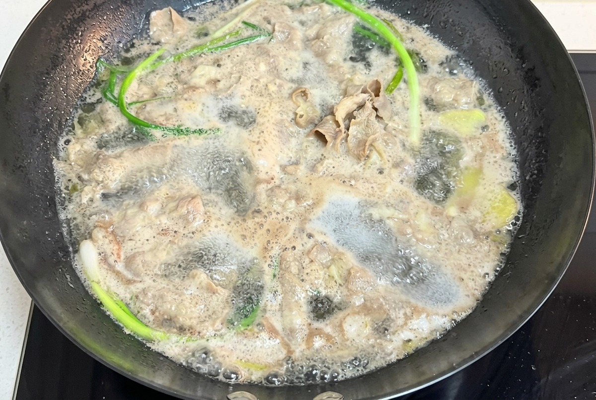 Thinly sliced beef bubbling in a pot of boiling water along with long green onion stalks.