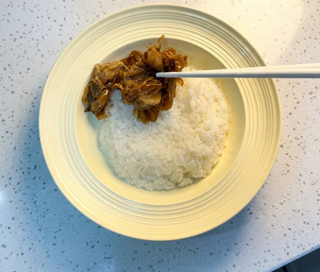 Chopsticks placing glazed beef and red onions onto a bowl of white rice.