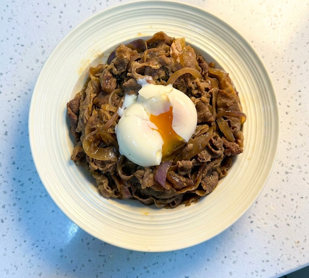 A Japanese beef bowl topped with a soft onsen egg with a runny orange yolk in the center.