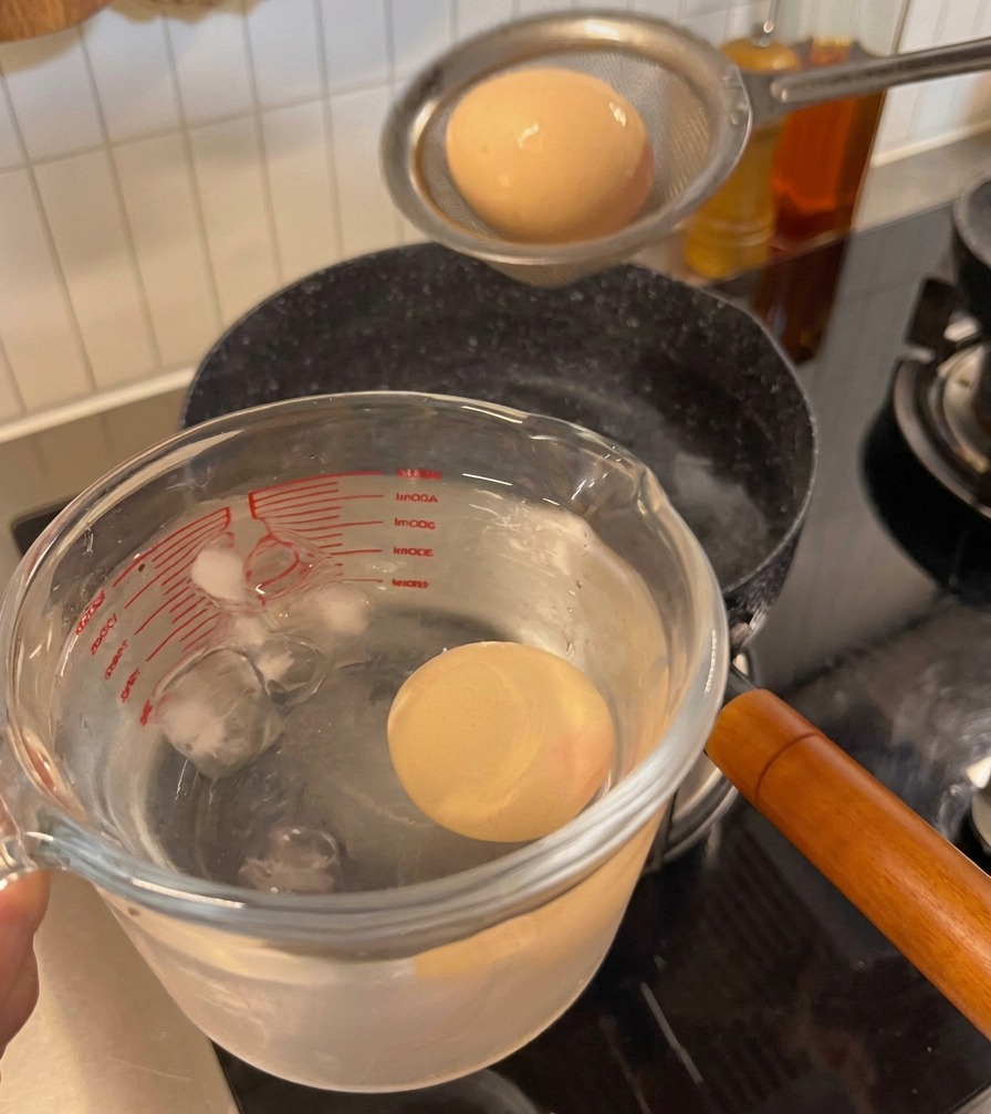 A cooked egg being moved from a strainer into a glass measuring cup filled with ice and water.