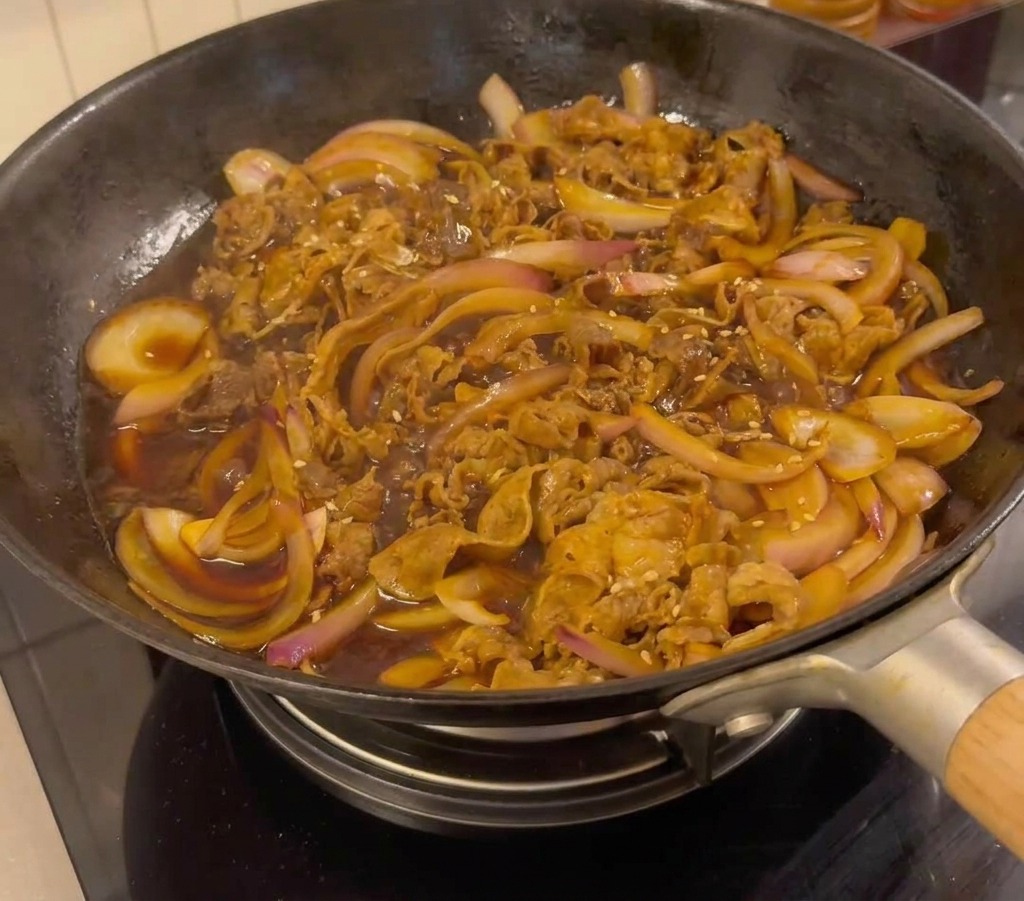 Finished teriyaki beef in a pan garnished with white sesame seeds and sliced green onions.