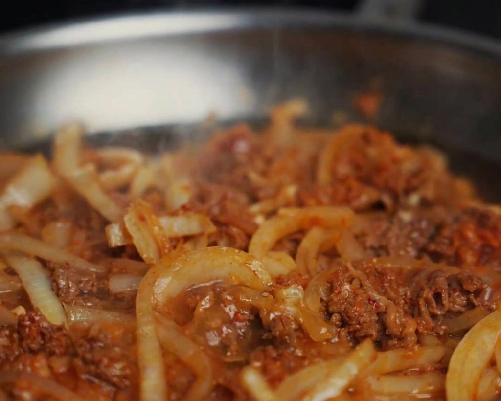 Water being added to a pan of stir-fried beef and onions, creating a bubbling sauce.