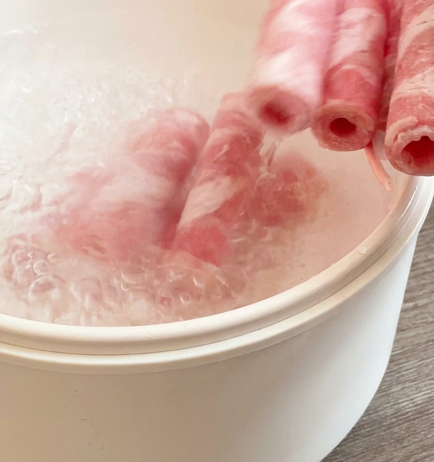 Slices of frozen beef rolls being submerged into a white pot of boiling water for a quick blanching.