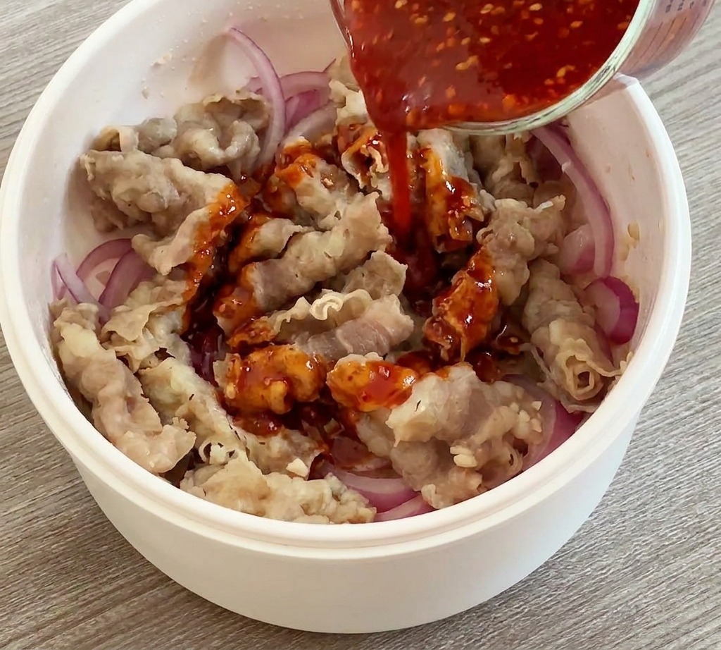 Pouring a vibrant red sauce from a measuring cup over cooked beef and onions in a white pan