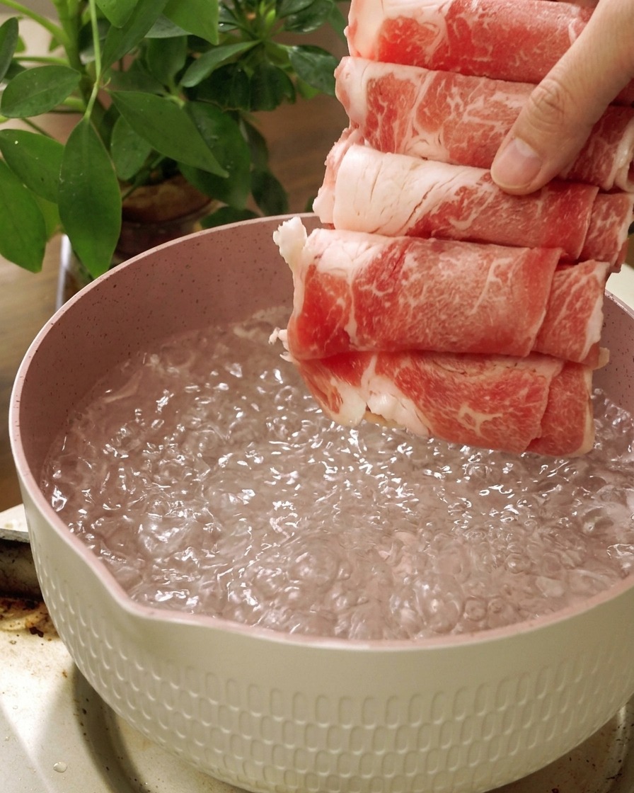 Slices of raw fatty beef being dropped into a pot of boiling water.