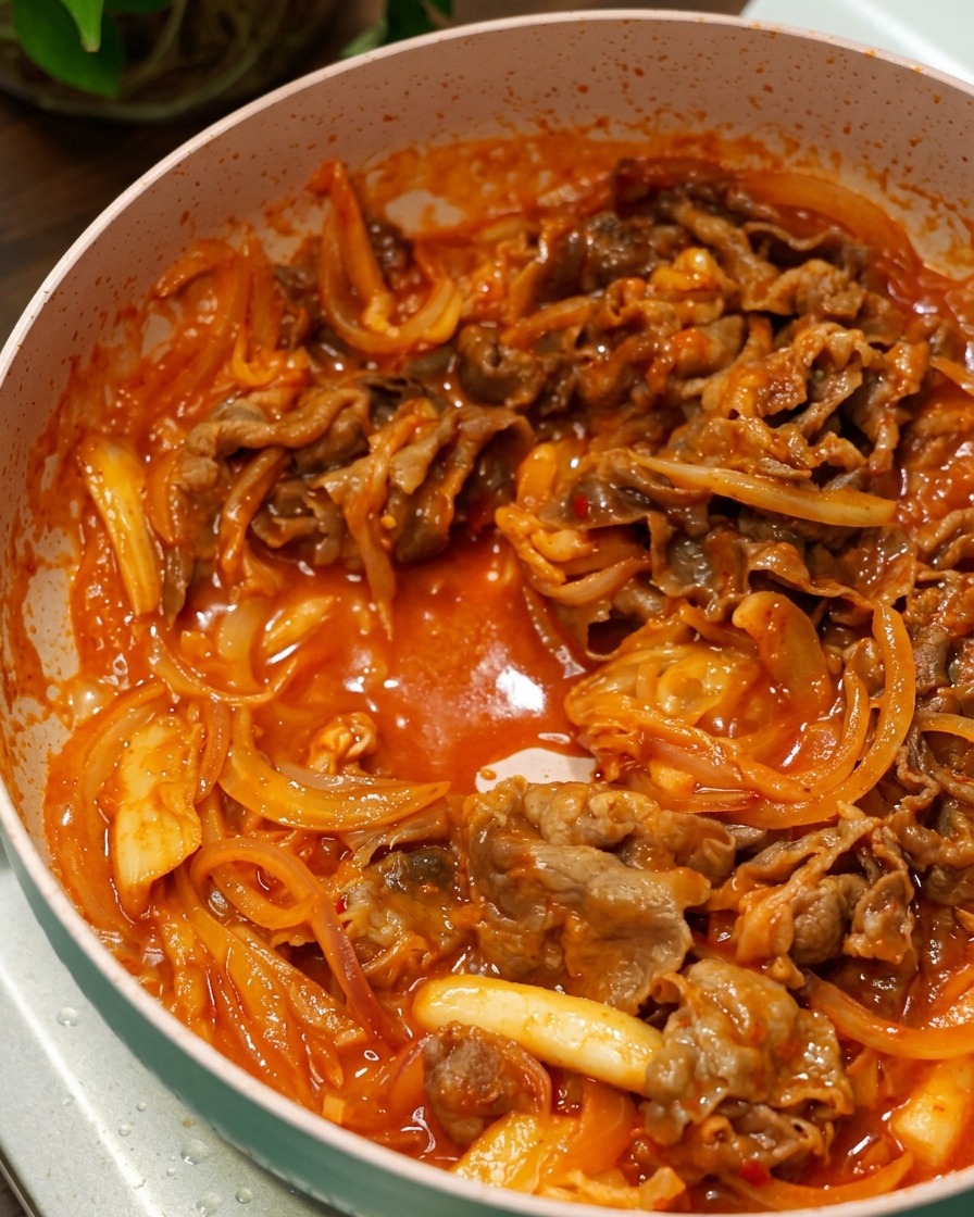 Beef and onions stir frying in a bubbling rich red Korean chili sauce inside a pink pan