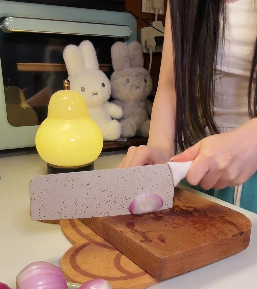 A person using a large kitchen knife to thinly slice small red onions on a bear-shaped wooden cutting board.