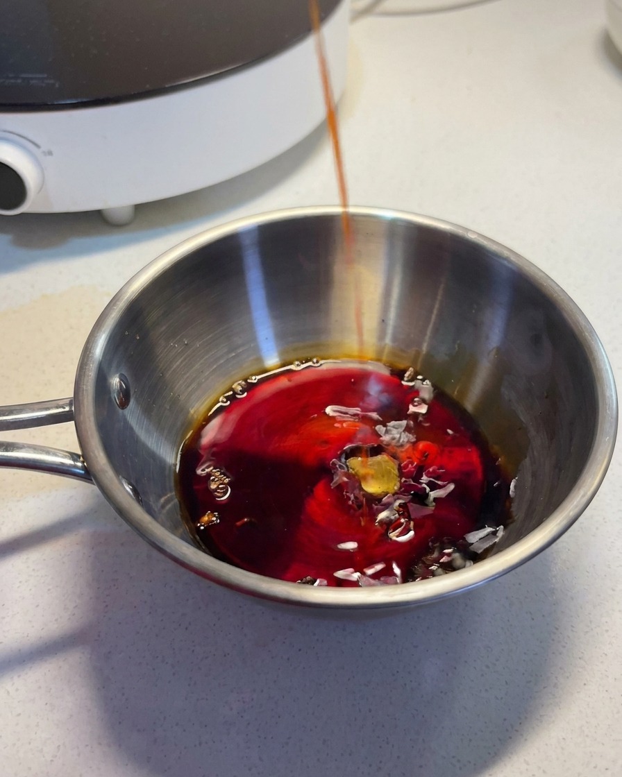 A dark, savory liquid being poured into a stainless steel bowl containing other sauce ingredients.