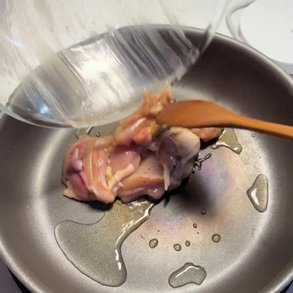 Seasoned chicken pieces being cooked in a hot pan with oil, with the surfaces starting to brown.