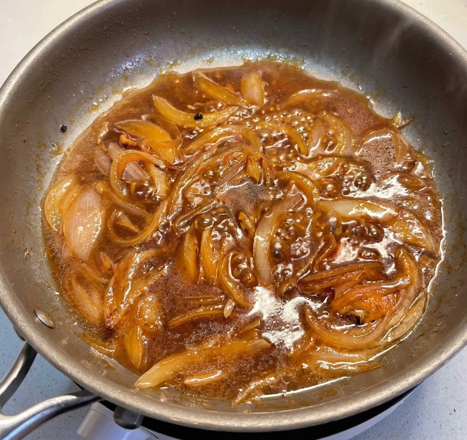 Slices of green leeks being added to a bubbling dark savory sauce filled with softened onions in a stainless steel pan.