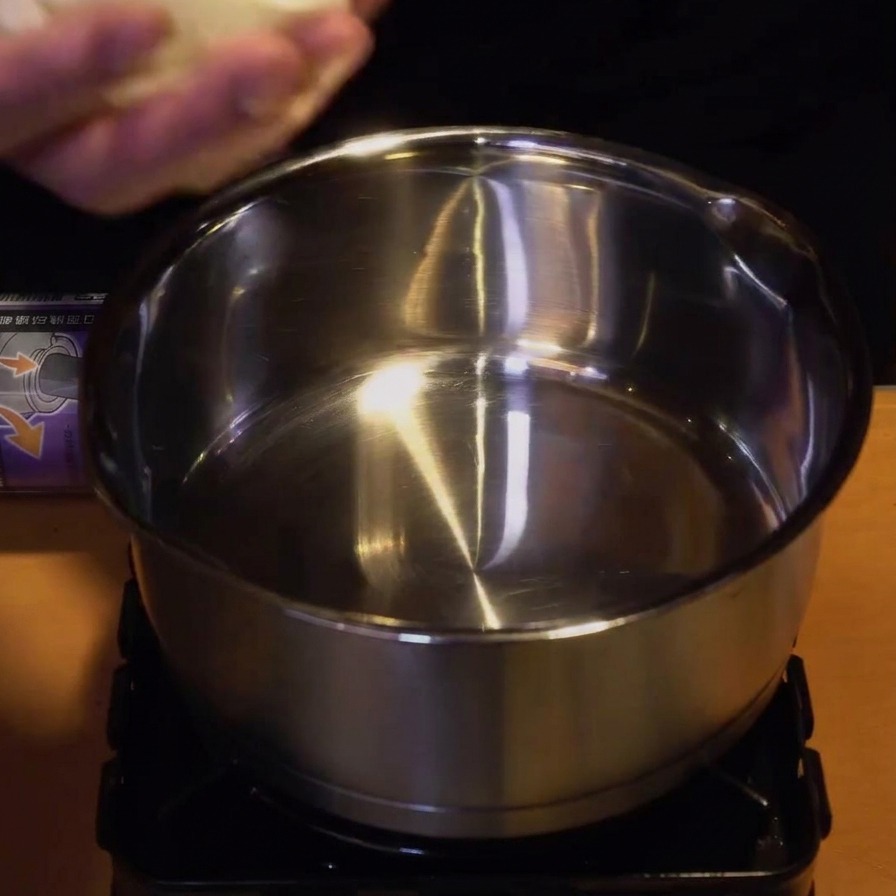 A person adding sliced raw onions and raw chicken pieces into a small stainless steel pot on a portable stove.