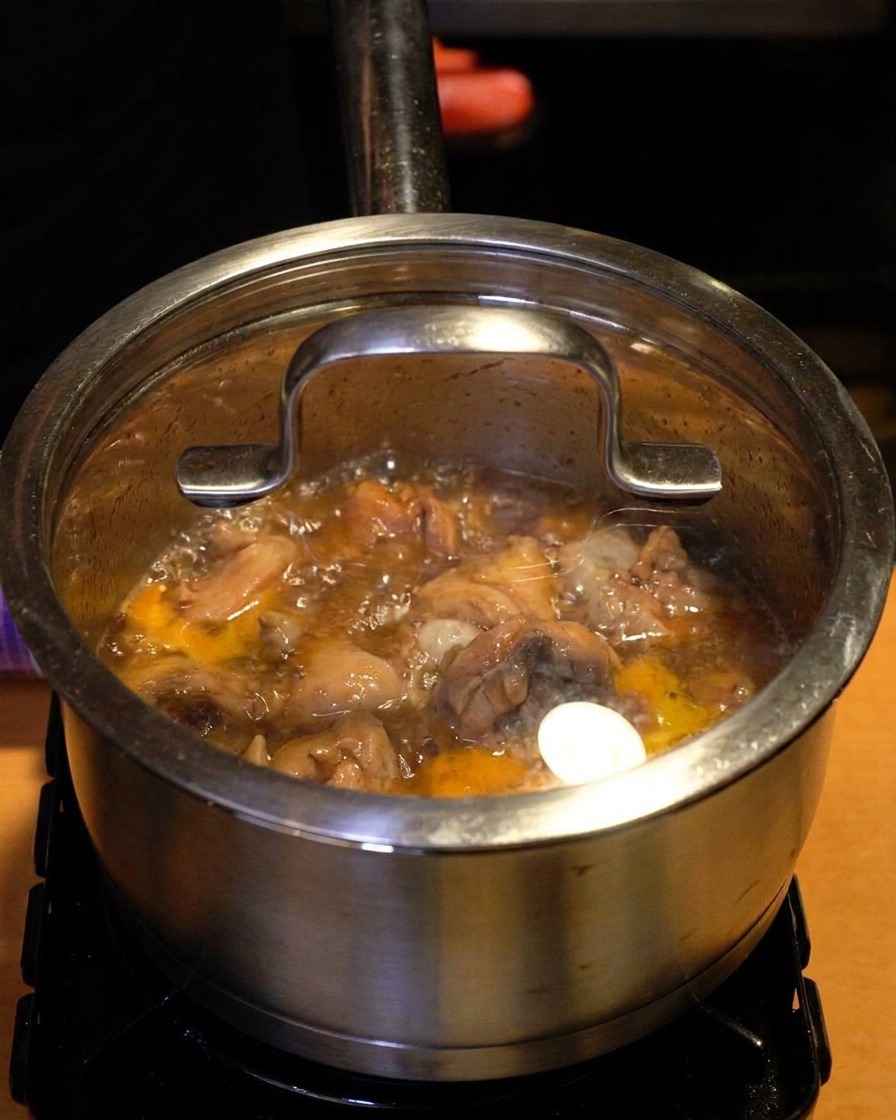 A stainless steel pot with a clear glass lid on top with steam and bubbling liquid visible through the glass.