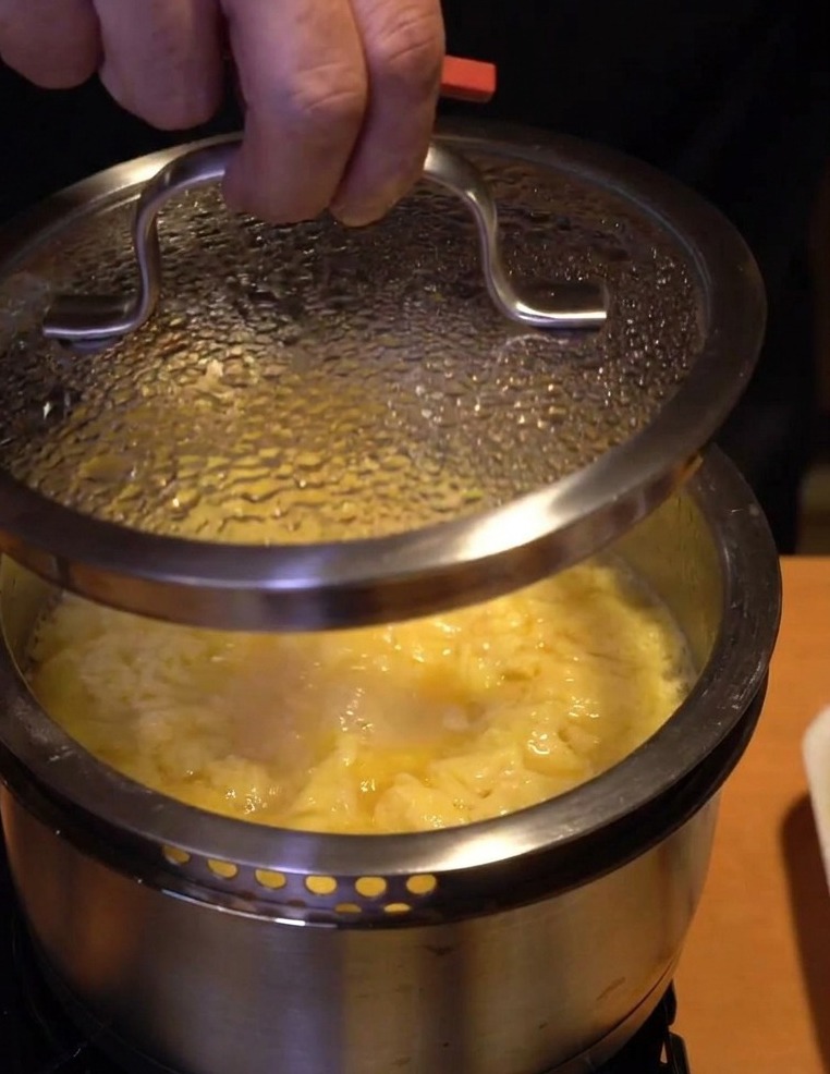 A close-up shot of a hand placing a glass lid over a pot of simmering chicken and eggs to let them set off the heat.