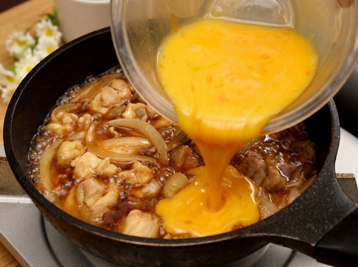 A stream of beaten egg being poured from a glass bowl into a frying pan with chicken and onions simmering in a dark saucecite: 4.