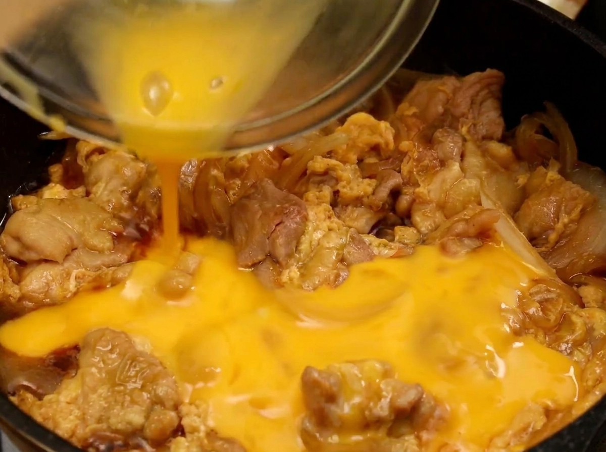 The final portion of yellow beaten egg being poured over the partially cooked egg and chicken in the pancite: 4.