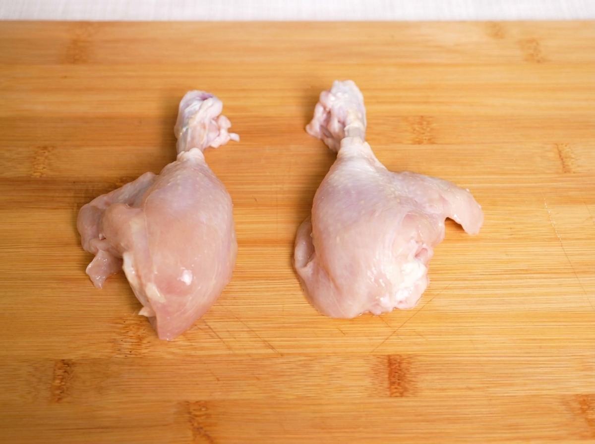 Raw chicken drumsticks placed on a wooden cutting board, ready to be sliced.