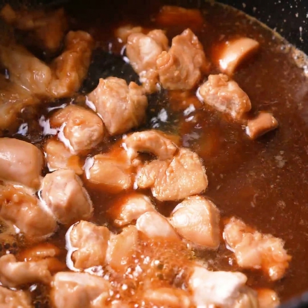 Chicken pieces simmering in a bubbling brown dashi broth inside a dark pan.