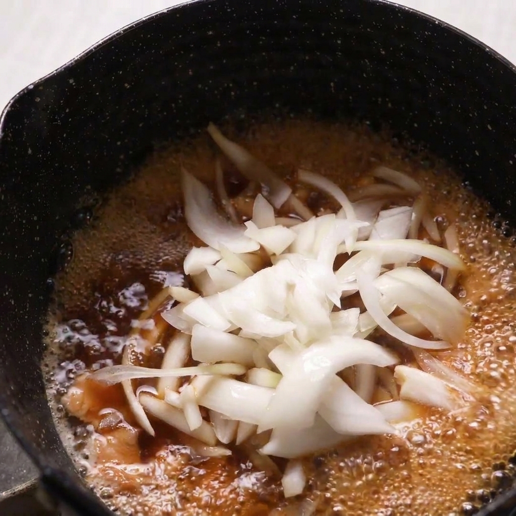 Thinly sliced raw onions being added to a simmering pan of chicken and dashi broth.