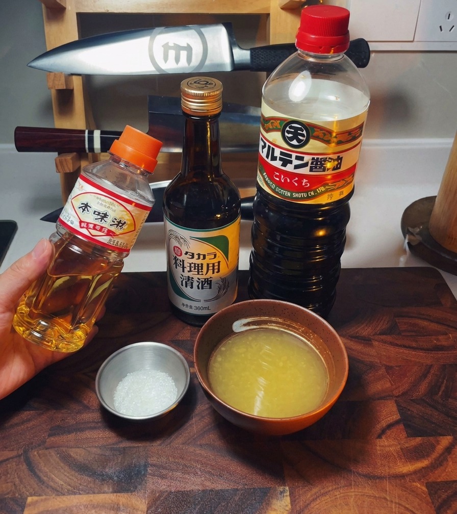 An arrangement of mirin, sake, and soy sauce bottles alongside a bowl of chicken broth and sugar.