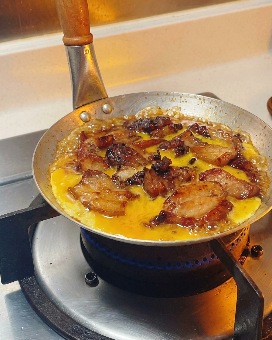 Beaten egg mixture being poured in a circular motion over chicken and onions simmering in a sauce.