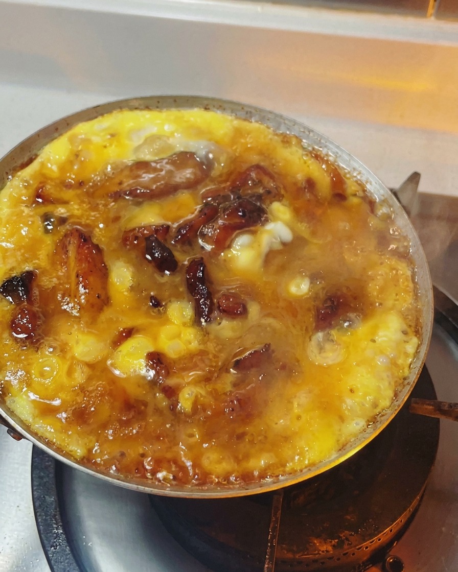 Oyakodon in a pan with the eggs cooked to a soft, semi-solid, and glossy texture over a bed of chicken and onions.