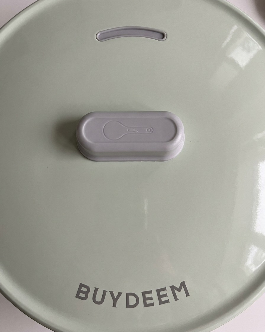 The light green lid of a modern rice cooker being closed to begin the cooking process.