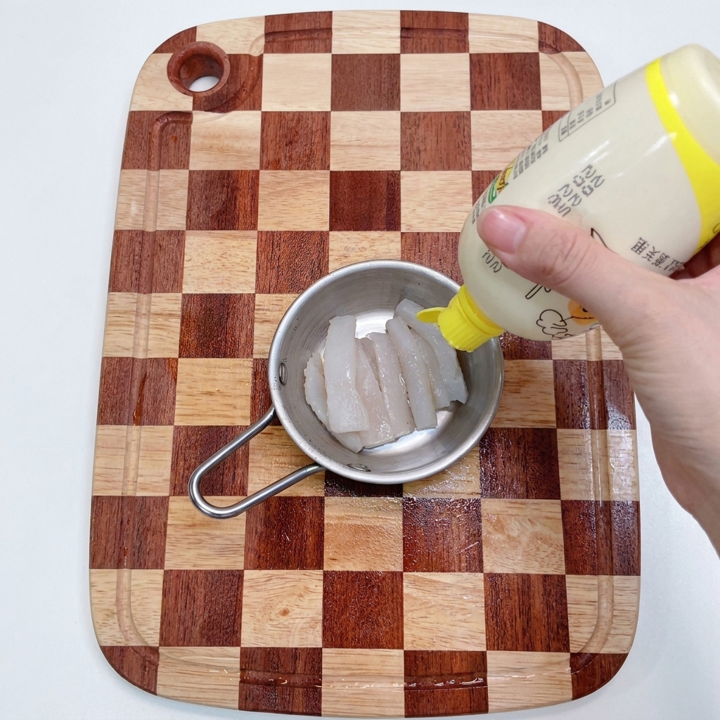 A person squeezing lemon juice from a yellow-capped bottle onto raw white cod strips in a stainless steel bowl.
