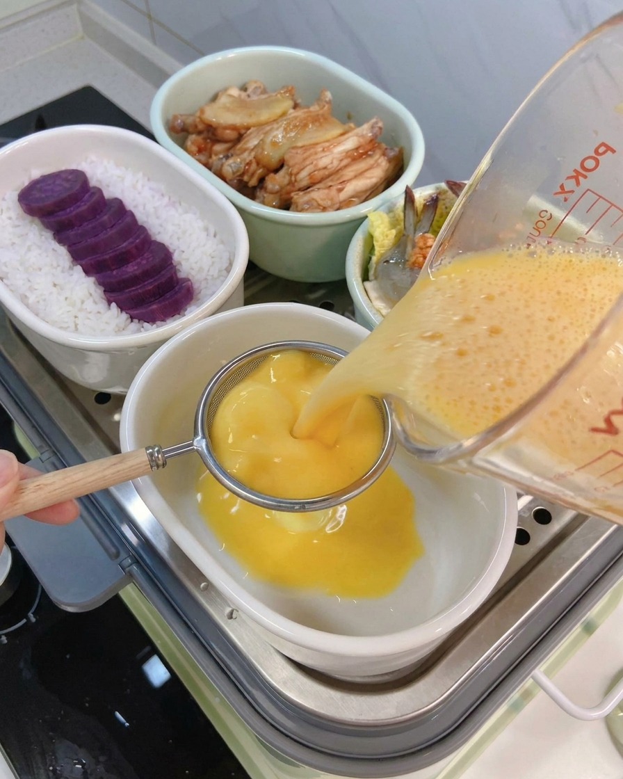 Yellow egg mixture being poured from a glass measuring cup through a metal sieve into a ceramic bowl.
