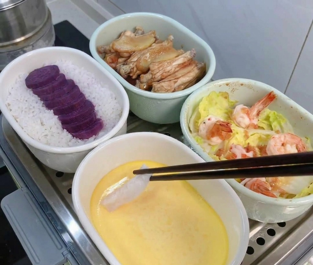 A hand using chopsticks to place a pale, marinated strip of cod onto the smooth, yellow surface of a partially set steamed egg custard.