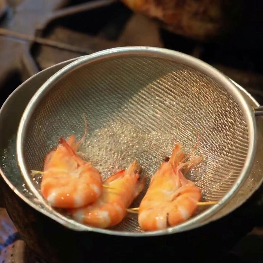 Three whole shrimp being boiled in a shallow metal mesh strainer inside a pot of bubbling water.