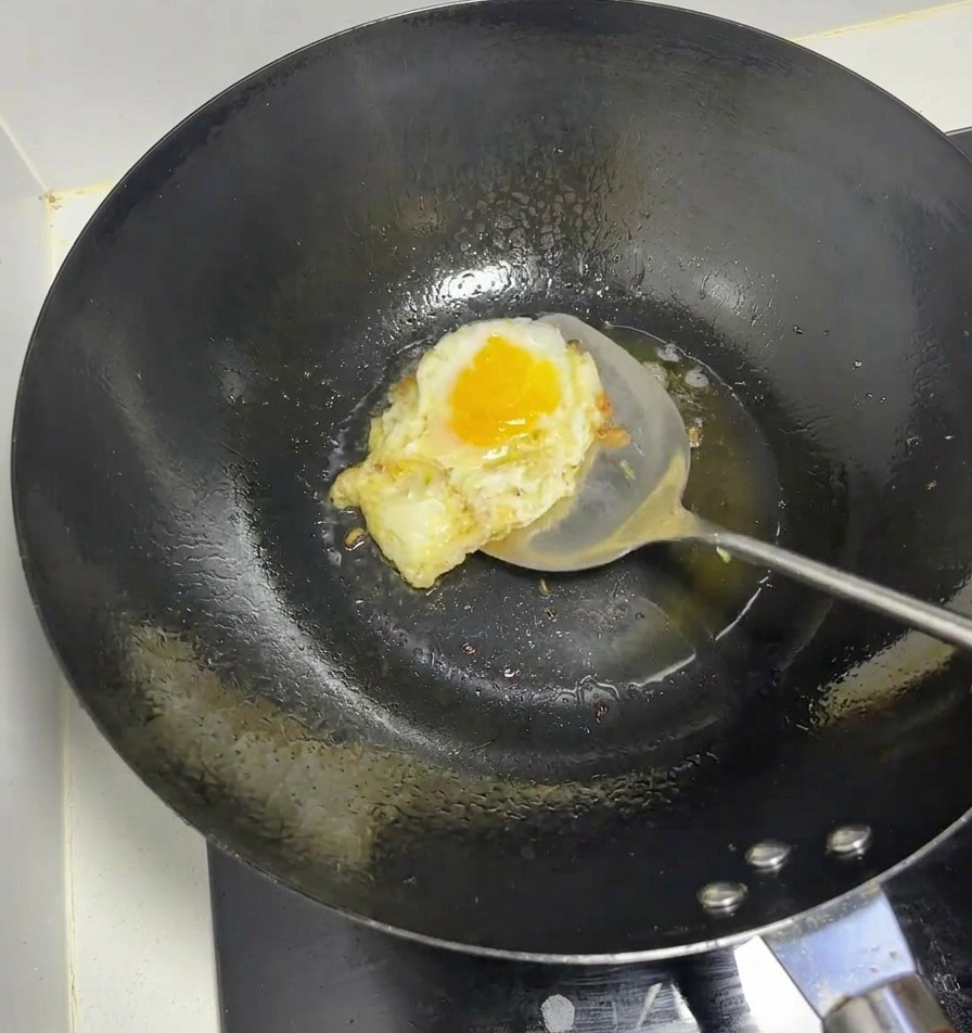 An egg being fried in a hot black wok using a metal spatula.