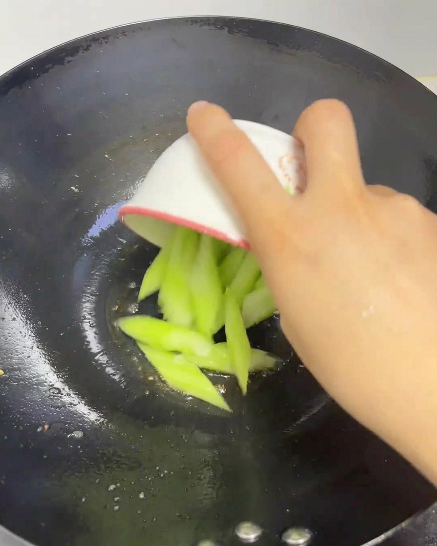 Fresh green silk melon slices being added from a small bowl into a heated wok.