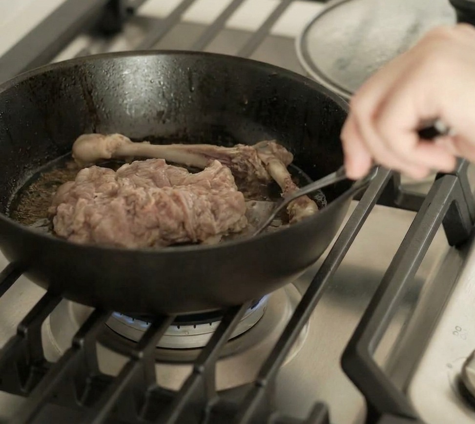 The duck leg being flipped over in a skillet, showing a perfectly seared and browned skin surface.