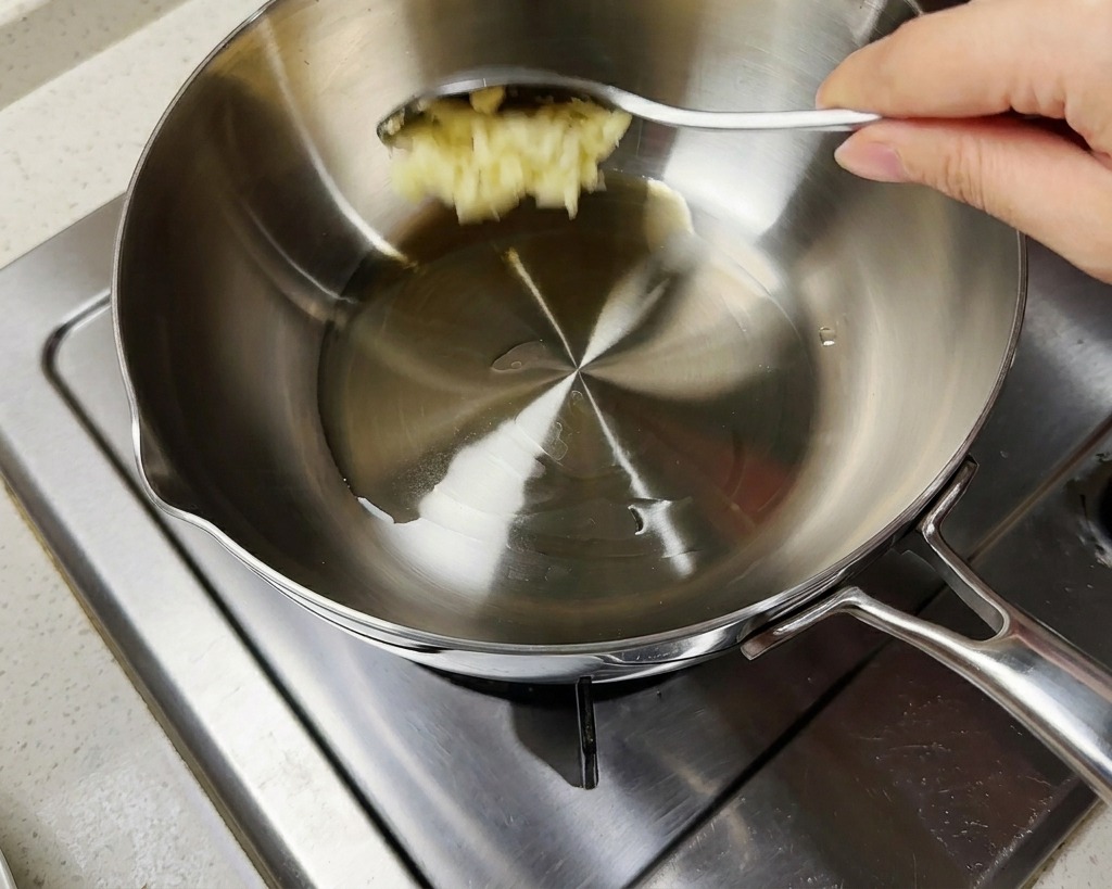 A spoonful of minced garlic being added to a pot containing hot oil and chopped green scallions.